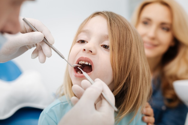 Merveilleux et agréable médecin examinant les dents de ses petits patients tout en utilisant des outils spéciaux lui offrant une meilleure vue