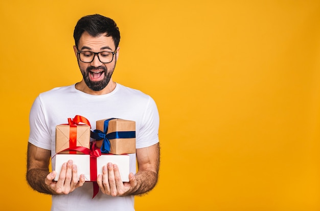 Merveilleux cadeaux! Adorable photo d'un homme barbu attrayant avec un beau sourire tenant des boîtes de cadeau d'anniversaire isolés sur fond jaune.