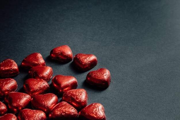 Photo de merveilleux cœurs de chocolat rouge éparpillés sur le noir