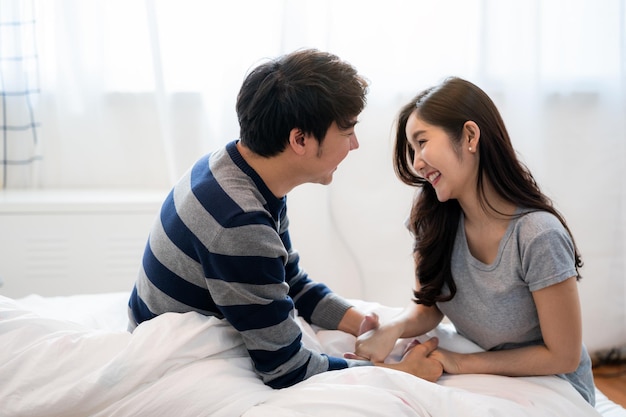 Merveilleux jeune couple asiatique sur le lit dans la chambre câlin et profiter de la vie ensemble et souriant tendre couple serrant dans son lit le matin avec bonheur