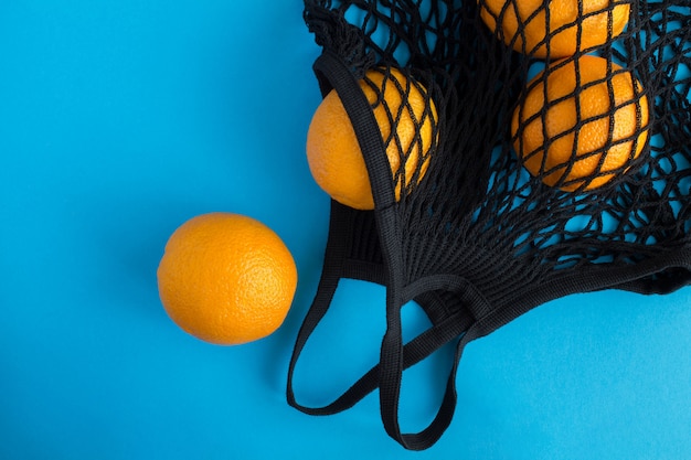 Mesh shopping sac noir avec des oranges sur le fond bleu