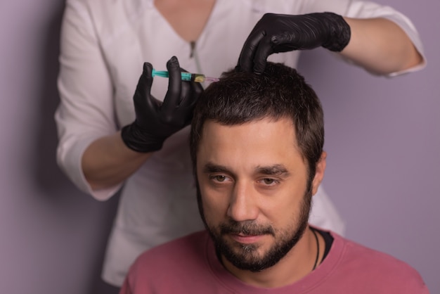 Mésothérapie pour les cheveux. Homme séduisant recevant des injections dans la tête. Homme ayant une séance de mésothérapie au salon de beauté, thérapeute en gant de protection avec seringue,