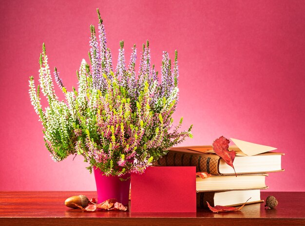 Message d'automne. Nature morte avec carte vierge rouge, enveloppe, fleurs de bruyère, feuilles sèches et livres