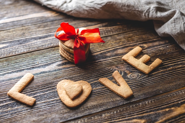 Message d'un biscuit sucré en forme de coeur et le mot amour et un cadeau attaché avec un ruban rouge sur fond de bois foncé