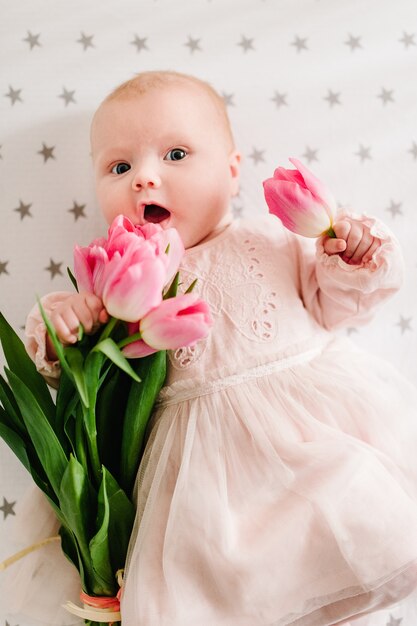 Message de la fête des mères avec la petite fille nouveau-née qui tient la fleur et couchée sur un lit avec un bouquet de tulipes roses.
