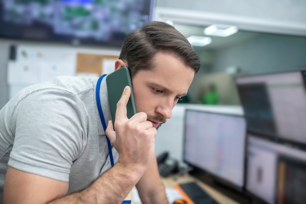 Message important. Attentif jeune homme barbu travaillant dans une salle spécialement équipée recevant des informations importantes par smartphone