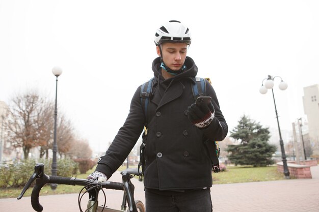 Messager mâle à l'aide de téléphone intelligent marchant avec son vélo dans la ville