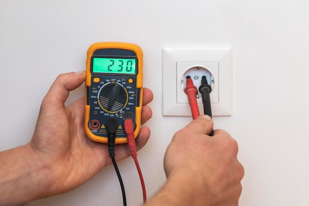 Mesure de tension par testeur dans la prise. Technicien électricien mesure la tension avec le testeur