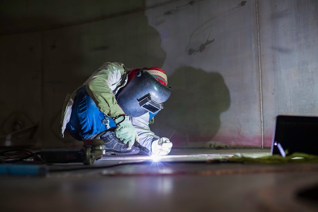 Le métal réparé par un travailleur à l'arc à l'arc de soudage est une étincelle de soudage dans un réservoir de construction industrielle d'huile inoxydable à l'intérieur d'espaces confinés