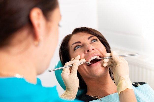 Mettre des attelles dentaires sur les dents de la femme au cabinet dentaire. Un dentiste examine une patiente avec un appareil dentaire en cabinet dentaire. Gros plan, jeune, séduisant, fille, bretelles, dents