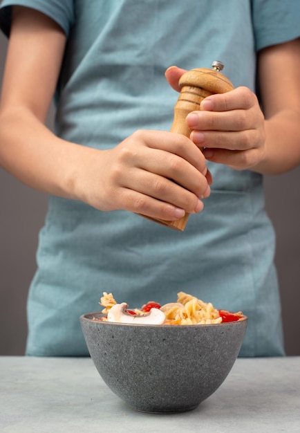 Mettre du poivre dans une salade de pâtes, des tranches de champignons, des tomates, des morceaux de poivre rouge et du thon.