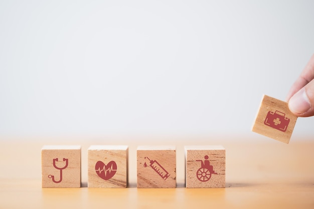 Mettre et empiler à la main un cube de blocs de bois qui imprime des icônes de soins de santé et médicaux à l'écran pour un concept de santé et de bien-être.