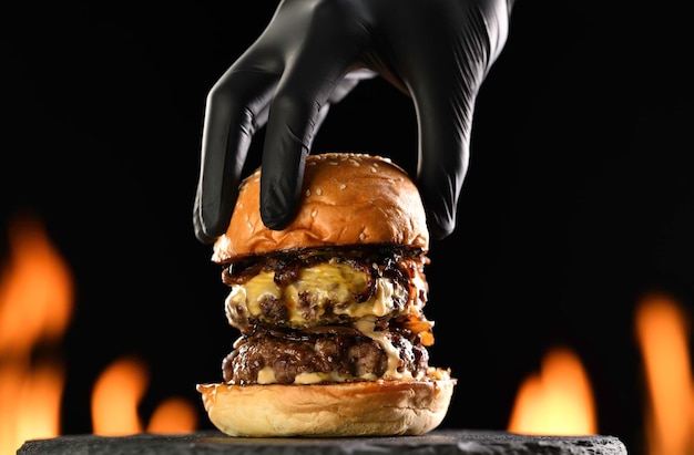 Mettre à la main le pain à hamburger supérieur sur un double cheeseburger à la viande avec de l'oignon caramélisé avec de la sauce suintante et dégoulinant sur fond flamboyant