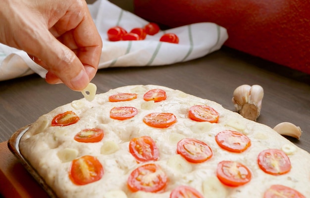 Mettre à la main une tranche d'ail dans la pâte pour la cuisson du pain focaccia à la tomate italienne et à l'ail