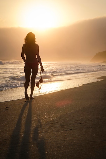 Mexique, Riviera Nayarit, silhouette de femme marchant dans le coucher du soleil sur une plage tout en tenant son bi