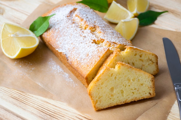 Miche de gâteau au citron sans gluten avec du sucre en poudre, des morceaux de citron, des feuilles vertes sur fond de bois rustique.