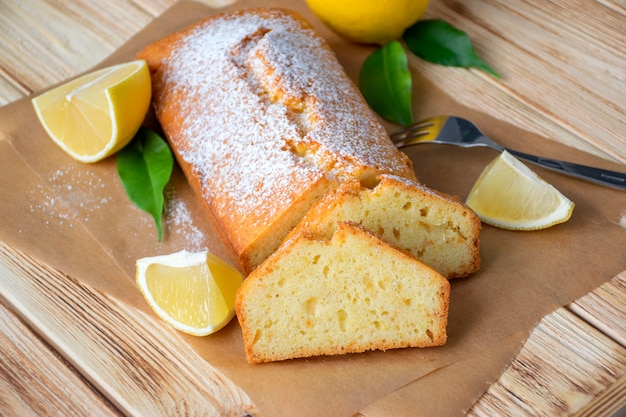 Miche de gâteau au citron sans gluten avec sucre en poudre, morceaux de citron, feuilles vertes