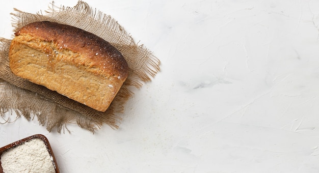 Une miche de pain rustique blanc sur une doublure en lin sur une table blanche. Idée de petite entreprise, cuire du pain au levain naturel sain sur commande. Vue de dessus avec espace copie