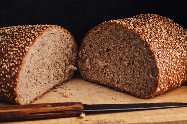 Une miche de pain saupoudrée de graines de sésame repose sur une planche à découper avec un couteau.