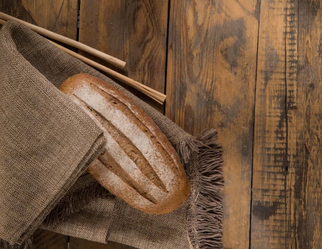 Une miche de pain sur une serviette et des épillets sur une surface en bois, vue d'en haut