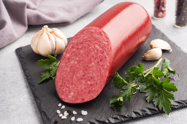 Une miche de saucisse Servelat salami sur une planche à découper avec du persil et des épices et de l'ail.