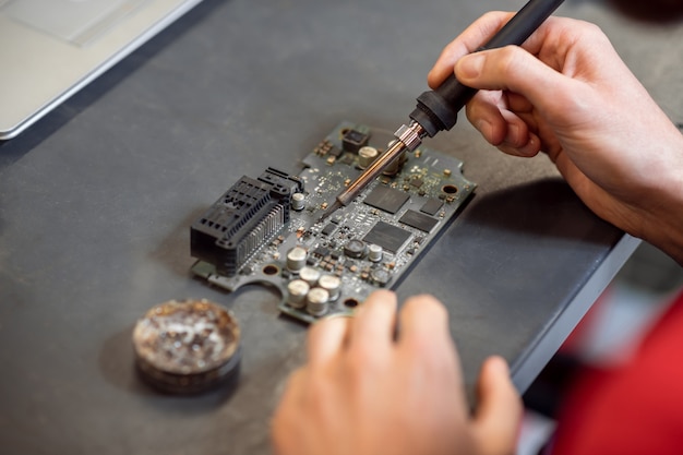 Microcircuit de soudure. Mâle expérimenté des mains avec des pièces de fer à souder fer à souder à chaud sur microcircuit à la table de travail.