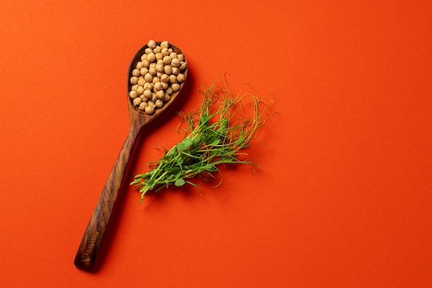 Microgreens et pois chiches dans une cuillère en bois sur fond orange foncé