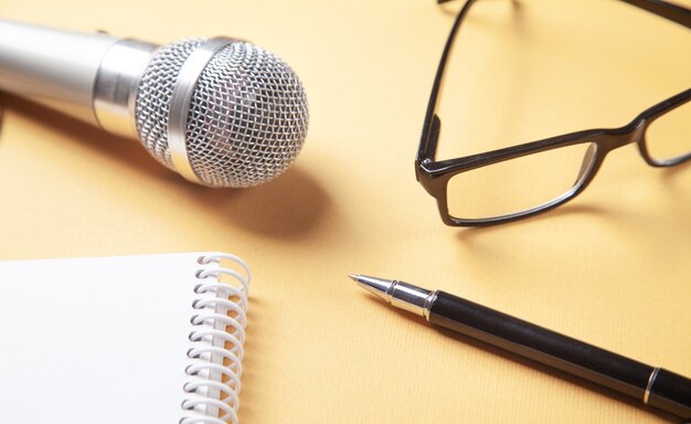 Microphone, bloc-notes, stylo, lunettes sur la surface jaune.