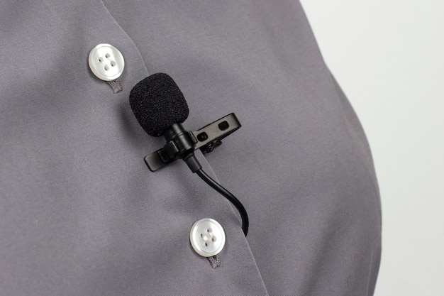 Le microphone cravate est fixé avec un clip sur un gros plan de chemise femme grise. Enregistrement audio du son de la voix sur un microphone à condensateur.