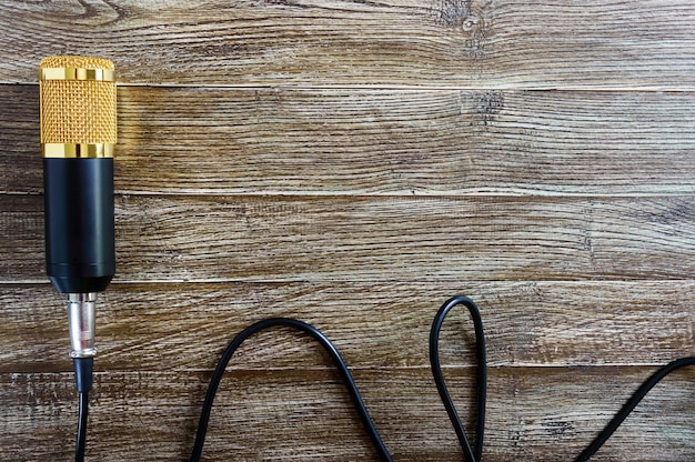 Microphone d'or à condensateur avec câble se trouve sur une table en bois avec espace de copie. Thème musical. Mise à plat. Vue de dessus.