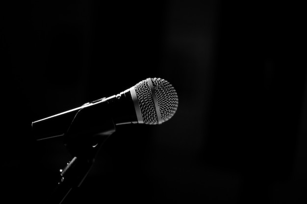 Le microphone de la scène se dresse sur un socle sur fond noir. Photographie en noir et blanc.