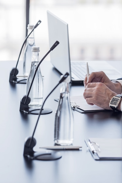 Microphones sur table dans la salle de conférence et mains d'homme d'affaires