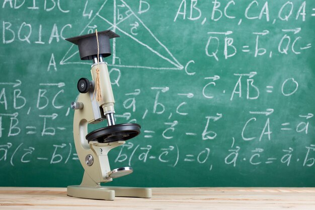 Microscope de concept d'éducation dans un chapeau de graduation sur le bureau dans l'arrière-plan du tableau noir de l'auditorium