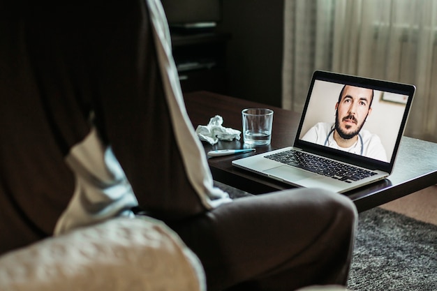 Mid adult man discuter de la médecine avec le médecin au cours d'un appel vidéo via un ordinateur portable alors qu'il était assis à la maison