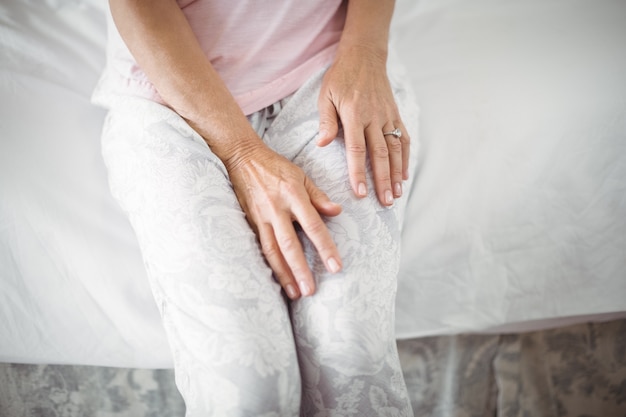 Mid-section of senior woman sitting on bed