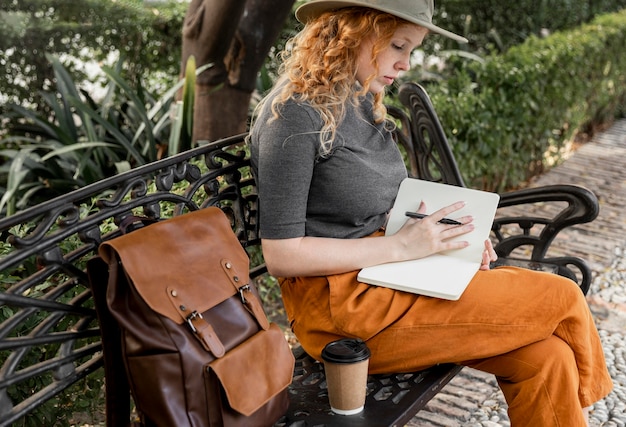 Photo mid shot femme sur banc écrit dans le journal