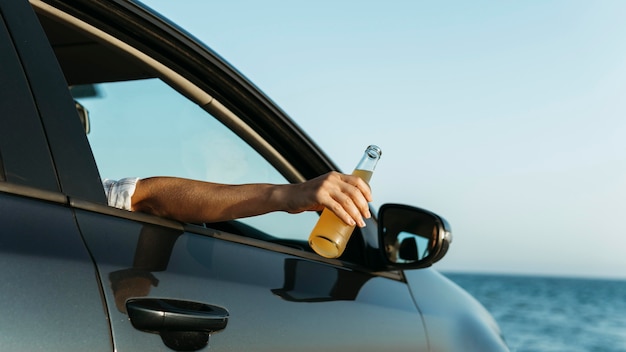 Mid shot woman holding bouteille de jus à l'extérieur de la fenêtre de la voiture