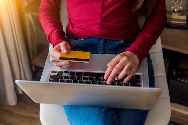 Midsection d'une femme utilisant un ordinateur portable tout en tenant une carte de crédit à la maison