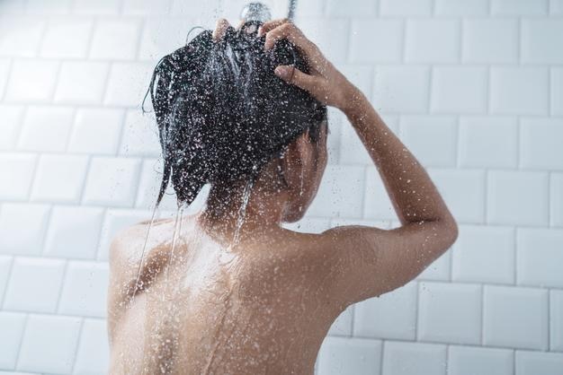 Midsection d'une jeune femme topless prenant une douche dans la salle de bain
