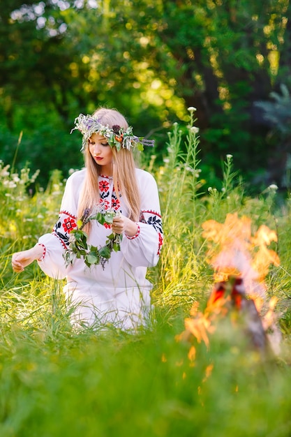 Midsummer. Femme tissant une couronne près du feu.