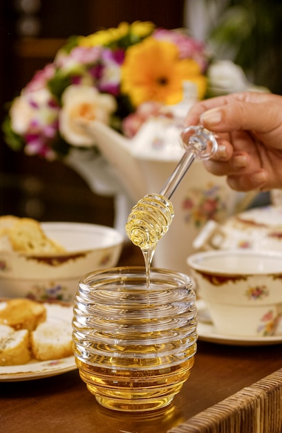 Miel d'abeille dans un récipient en verre et mains tenant du miellat sur une table dressée avec un style vintage