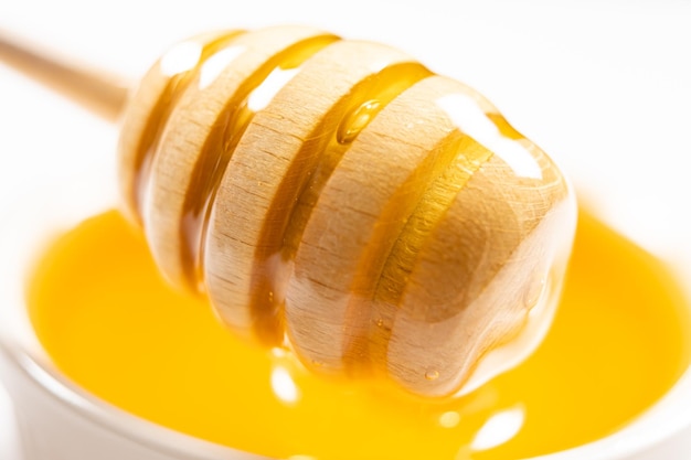 Miel d'abeille naturel liquide dans un bol en céramique blanche avec une cuillère en bois