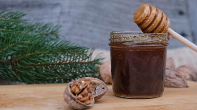 Photo miel biologique fait maison brun foncé dans un bocal en verre avec un bâton de miel sur un fond rustique avec des noix