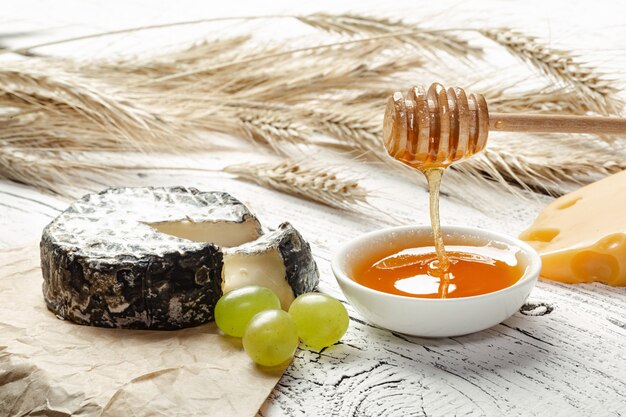 Le miel coule dans un bol près du fromage, des noix et des épis de blé