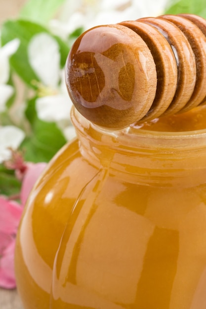 Miel dans un bocal en verre et bâton avec des fleurs en fleurs