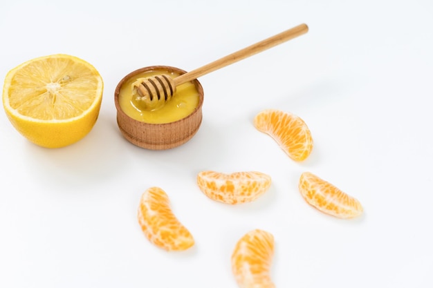 miel dans un bol en bois et orange sur fond blanc.