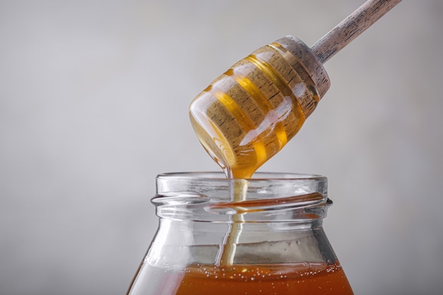 Miel dégoulinant de miel louche dans un bocal en verre.. Gros plan. Miel épais organique sain trempant de la cuillère en bois de miel, plan rapproché.