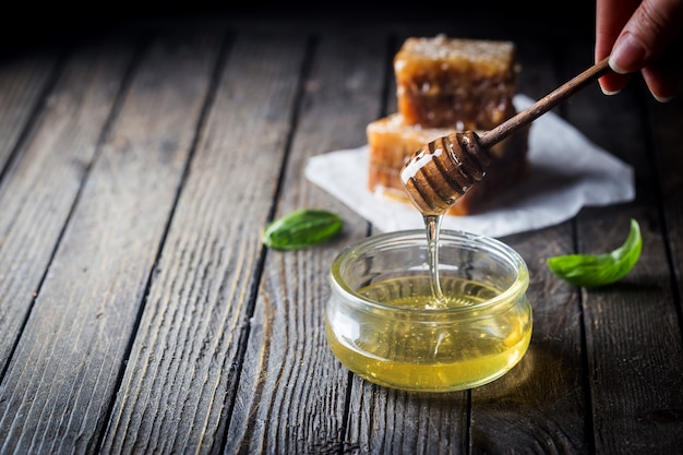 Miel dégoulinant de miel louche dans un bocal en verre avec nid d'abeille sur fond sombre.