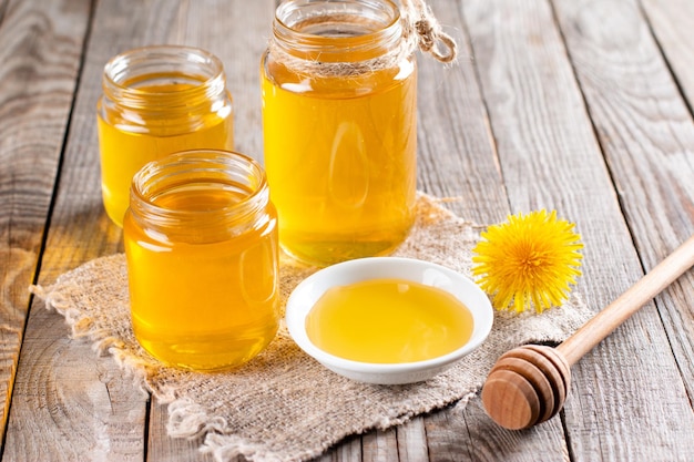 Miel de fleurs dans un bocal en verre et pissenlits sur une table en bois