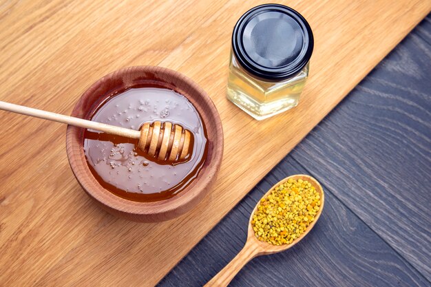 Miel de fleurs fraîches de différentes variétés, pollen avec cuillères sur fond de bois. Aliments de santé aux vitamines biologiques